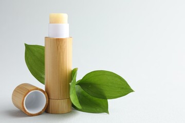 Lip balm and leaves on white background, closeup. Space for text