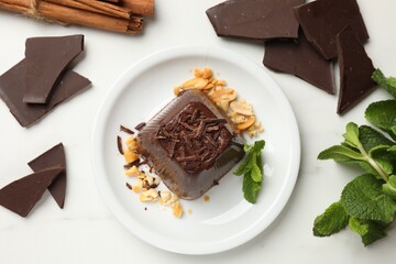 Tasty chocolate pudding with peanuts and mint on white table, flat lay
