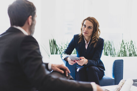 Businesswoman and businessman sitting in armchairs in office talking