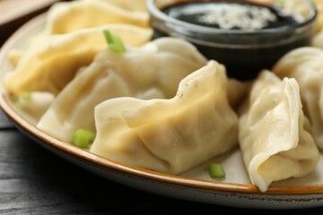 Tasty boiled gyoza (dumplings) with green onion and soy sauce on black table, closeup
