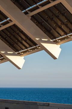 Large solar pergola in Barcelona overlooking the sea. Sustainable architecture integrating renewable energy in urban design.