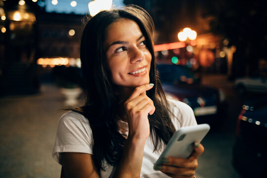 Young woman using smartphone in the city at night, looking up