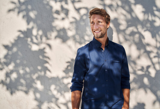Smiling young man outdoors with shadow of leaves at the wall