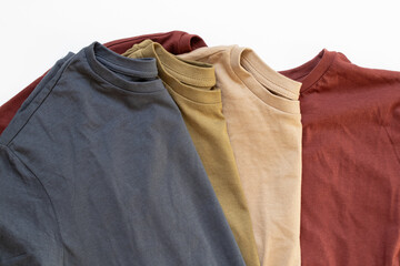Four cotton crumpled T-shirts blue and beige and olive and red lie on a white background, clothes,...