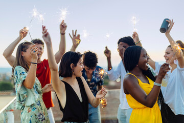 Group of happy multi-ethnic friends celebrating a party in the evening, holding sparklers