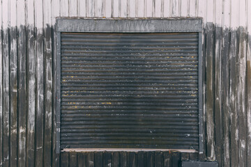 Weathered metal shutter on a wooden wall showcases urban decay and industrial charm in late afternoon light