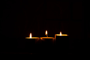Three homemade candles in plaster candlesticks burn in the dark of the house, candle flame, candles