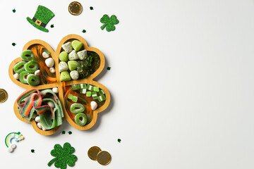 Patrick's Day candy assortment in a four-leaf clover-shaped tray, surrounded by festive decorations like glittery shamrocks, gold coins, and a leprechaun hat on a white background.