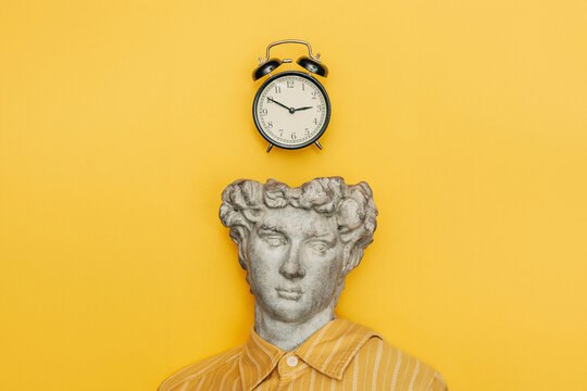 Classical bust with alarm clock on yellow background symbolizing time and urgency