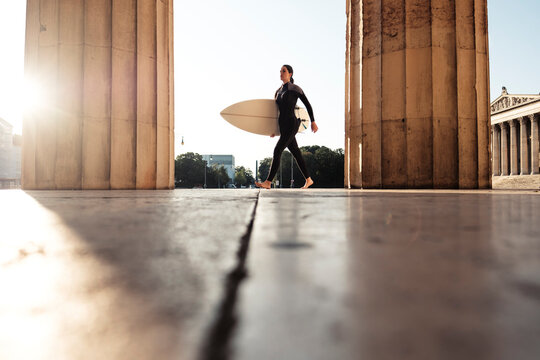 Young woman with surfboard on the way to Eisbach, Munich, Germany