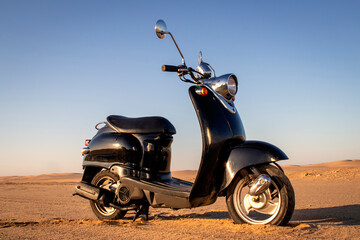The Retro black scooter at sunset in the golden sand of the Namib Desert