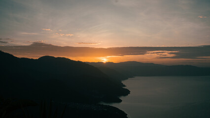 The sun rising behind majestic mountains, casting a warm glow over the tranquil lake