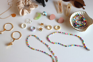 Hand figurine, sunglasses, gold jewelry, colorful bead jewelry, statement rings and various hair accessories on the white table. Selective focus.