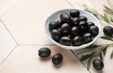 Black olives served in ceramic bowl on hexagonal beige tiles, decorated with olive tree branch