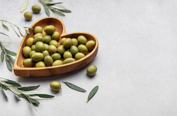 Fresh green olives displayed on wooden heart shaped bowl with olive branches