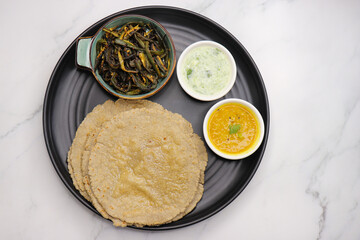 Roti and Sabzi. Indian vegetarian Thali includes bhindi fry, yellow daal tadka, cucumber raita, and jwari or jowar bhakri. Indian food is served in a plate or thali. Copy Space. healthy Veg Thali.