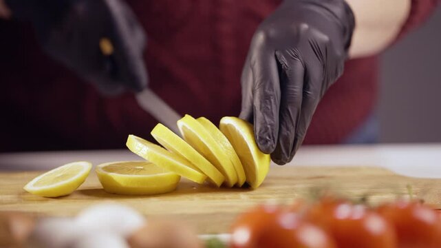 Close-up of hands in black gloves slicing a ripe lemon on a wooden board. The fresh citrus fruit is perfect for cooking, drinks, and garnishing meals, adding a zesty and refreshing touch to any dish