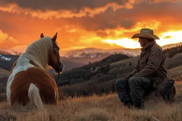 Fototapeten Cowboy relaxes with horse at sunset in mountainous landscape © ChaoticMind