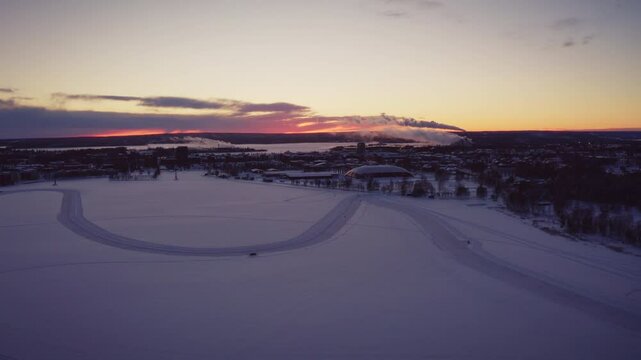 Winter Sunset over a Snow-Covered City with a Frozen Lake and Winding Ice Tracks, Smoke Rises from a Distant Factory, Trees and Buildings in Cold and Beautiful Landscape, Pite&aring;, Northern Sweden
