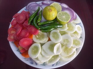 Chopped green mixed vegetables in a beautiful white plate, radish, carrot sliced, onion, lemon, salad in small pieces, radish, cucumber, green vegetables,,vegetable salad in plate
