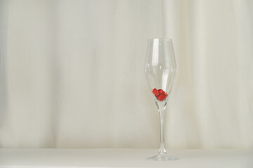 Wine glass with heart confetti on cream background. Minimalist holiday photo for Valentines