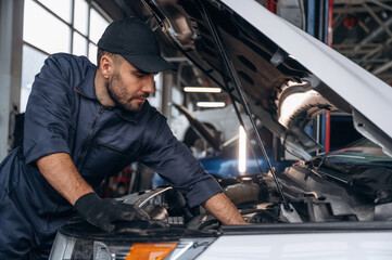 Fototapeta premium View from the side, opened hood. Mechanic working in a car service station