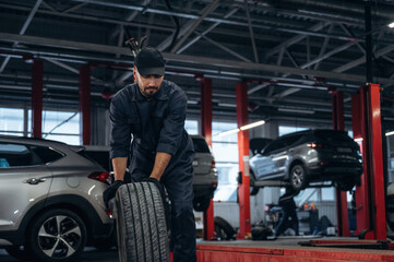 Fototapeta premium Moving the tire. Mechanic working in a car service station