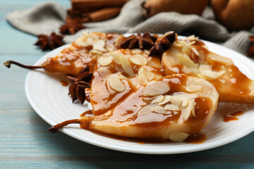 Delicious pears with caramel sauce, almond flakes and anise stars on light blue wooden table, closeup