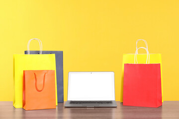 Internet shopping. Laptop and colorful paper bags on wooden table against yellow background