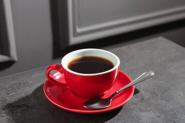 Red cup of aromatic coffee, saucer and spoon on dark textured table, closeup
