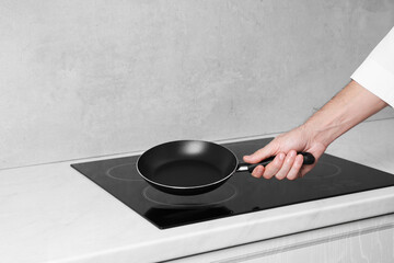 Chef holding frying pan over cooktop in kitchen, closeup
