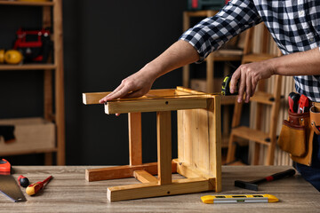 Repairman measuring wooden stool at table in workshop, closeup