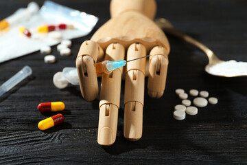 Drug addiction. Mannequin hand with syringe and pills on black wooden table, closeup