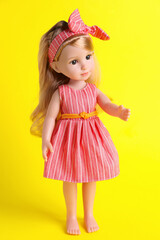 Beautiful doll in dress and headband on yellow background