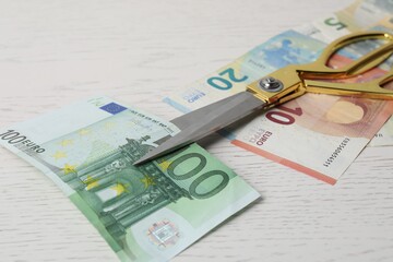 Euro banknotes and scissors on white wooden table, closeup