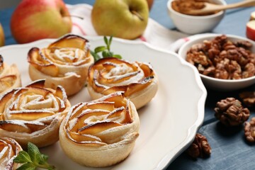 Tasty apple roses with powdered sugar served on blue wooden table, closeup