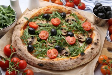 Tasty pizza with cherry tomatoes, black olives, mushrooms and arugula on table, closeup