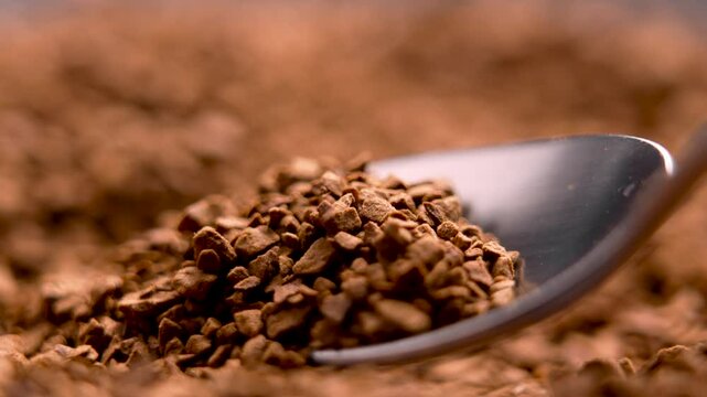 Granulated instant coffee on metallic spoon with blurred background of roasted granules. Strong aroma drink ingredient. Macro shot.