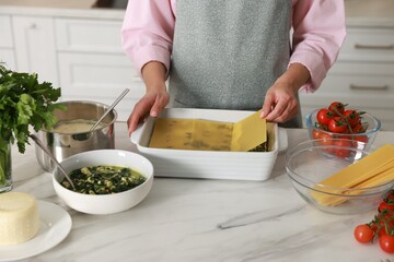Woman making spinach lasagna at marble table indoors, closeup