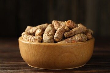 Tumeric rhizomes in bowl on wooden table, closeup
