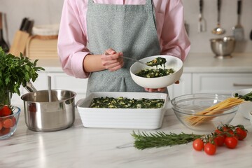 Woman making spinach lasagna at marble table in kitchen, closeup
