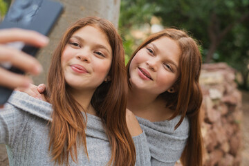 Twin sisters taking a selfie with a smartphone in a park