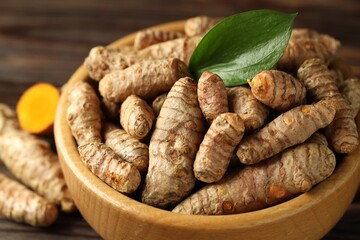 Tumeric rhizomes with leaf in bowl on table, closeup