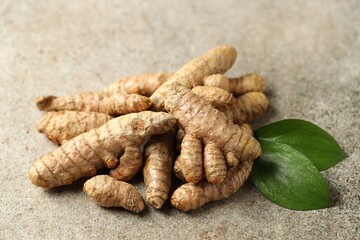Pile of tumeric rhizomes with leaves on grey table, closeup