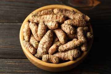 Tumeric rhizomes in bowl on wooden table, closeup