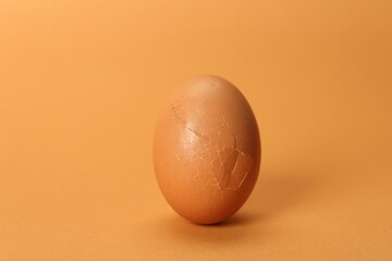 One egg with cracked shell on coral background, closeup