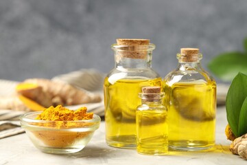 Turmeric oil, powder and green leaves on grey table, closeup