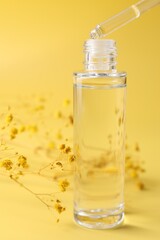 Dripping serum from pipette into bottle and gypsophila flowers on yellow background, closeup