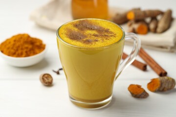 Tasty turmeric latte in cup and ingredients on white wooden table, closeup