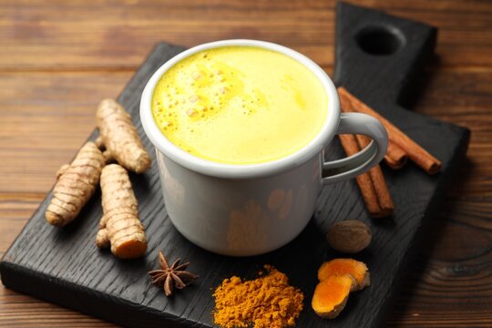 Tasty turmeric latte in cup and spices on wooden table, closeup